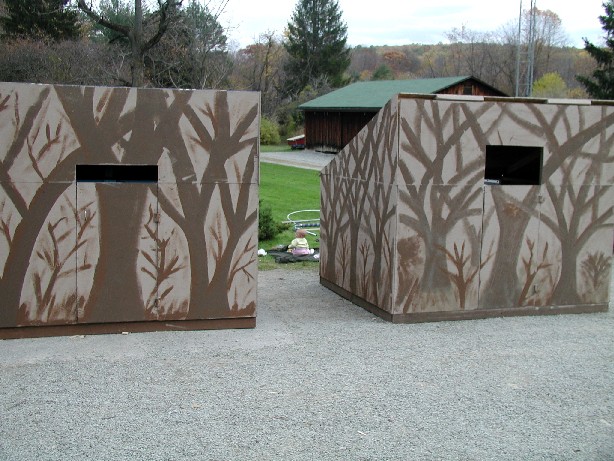 fully constructed blinds, wooden boxes with trees painted on them, large enough to hold a person
