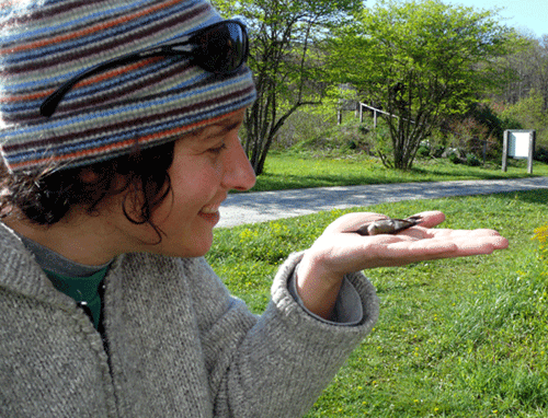 woman in a hat holding a Ruby-throated Hummingbird on her flat palm